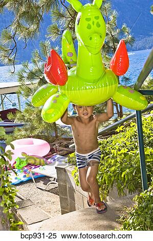 Stock Photography - boy carrying dragon floatie up from lake. Fotosearch