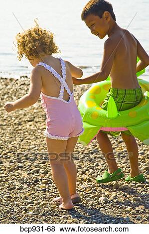 Stock Photo - boy helping girl walk on rocky beach. Fotosearch