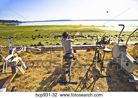 Stock Image - boy on exercise bike next to beach. Fotosearch