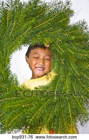Stock Photograph - boy peering through evergreen wreath. Fotosearch