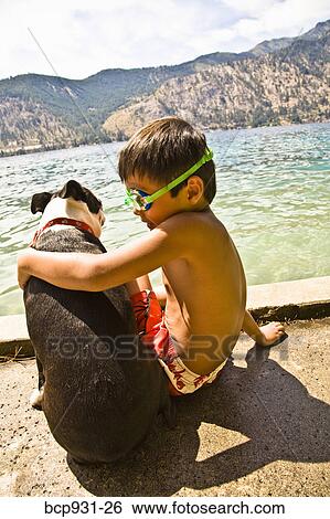 Stock Photograph - Boy sitting by lake with boston terrier dog. Fotosearch