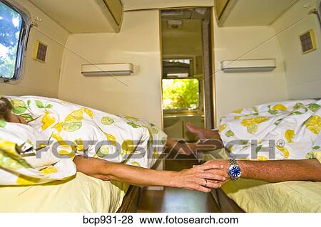 Stock Photo - couple holding hands in bed in camper. Fotosearch