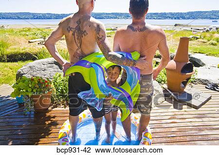 Stock Image - tattoed men and boy in wading pool at beach. Fotosearch