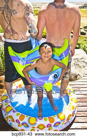Stock Image - tattoed men and boy in wading pool at beach. Fotosearch