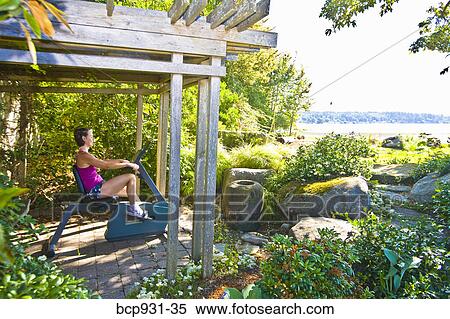 Stock Photography - woman on exercise bike near beach. Fotosearch
