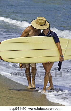 Stock Image - couple kissing behind surfboard. Fotosearch