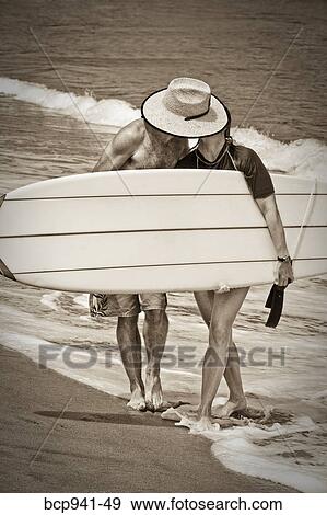 Stock Photo - couple kissing behind surfboard. Fotosearch