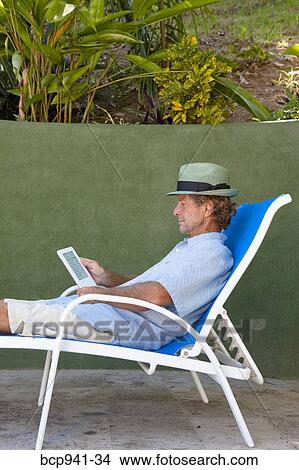 man reading e-book on chaise outdoors View Large Photo Image Picture - man reading e-book on chaise outdoors. Fotosearch