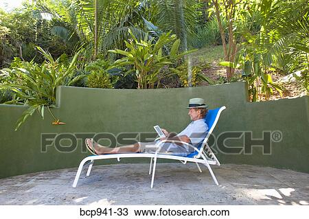 man reading e-book on chaise outdoors View Large Photo Image Stock Image - man reading e-book on chaise outdoors. Fotosearch