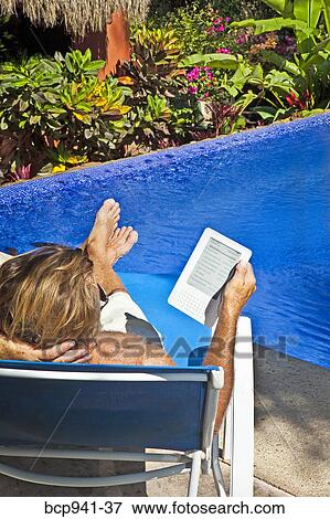 Stock Photo - man reading e-book on chaise outdoors. Fotosearch