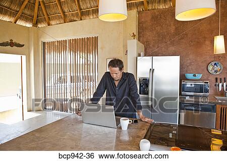 Stock Photograph - man working on laptop in kitchen. Fotosearch