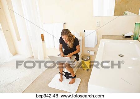 Stock Photo - woman on laptop in bathroom. Fotosearch