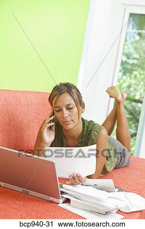 Stock Image - woman paying bills on couch. Fotosearch