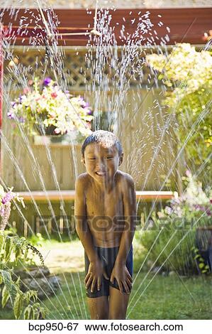smiling boy standing in sprinkler View Large Photo Image Stock Photo - smiling boy standing in sprinkler. Fotosearch