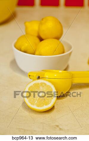 Stock Image - Bowl of lemons and lemon juicer on counter. Fotosearch