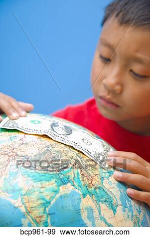 Stock Photo - Boy placing dollar bill on globe. Fotosearch