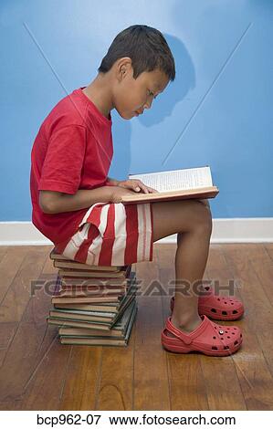 Stock Photo - Boy reading while seated on stack of books. Fotosearch