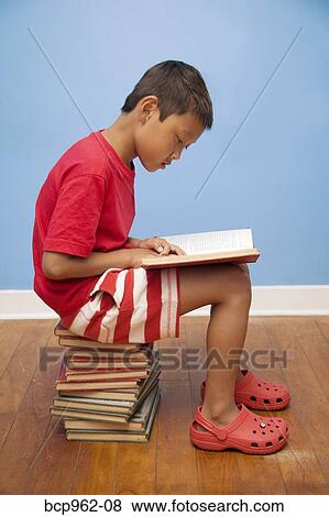 Boy reading while seated on stack of books View Large Photo Image Stock Photo - Boy reading while seated on stack of books. Fotosearch