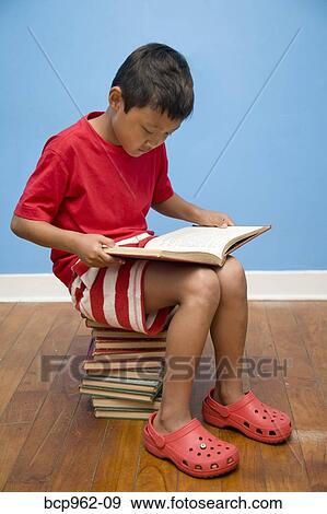 Boy reading while seated on stack of books View Large Photo Image Stock Photo - Boy reading while seated on stack of books. Fotosearch