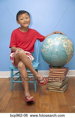 Stock Photograph - Boy seated next to globe resting on stack of books. Fotosearch