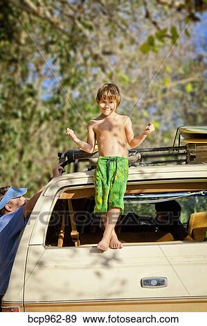 Stock Photo - Boy standing on back of car. Fotosearch