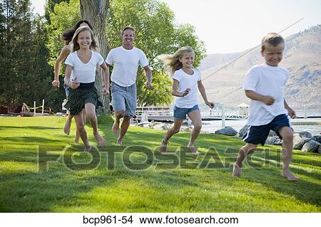 Picture - Family of five running in lakeside park. Fotosearch