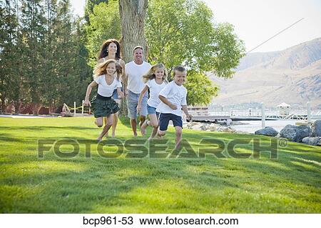 Stock Image - Family of five running in lakeside park. Fotosearch