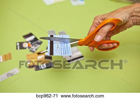 Stock Image - Hand using scissors to cut up credit cards. Fotosearch