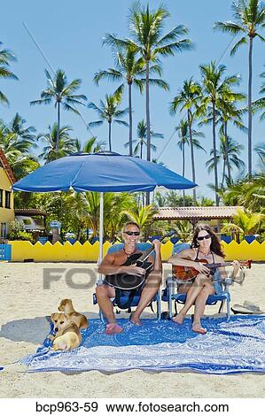 Stock Photo - Happy man and woman in beach chairs with guitars and dogs. Fotosearch