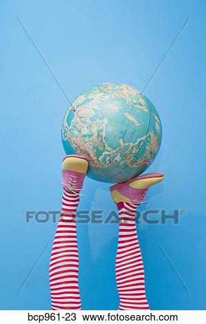 Stock Image - Legs in striped socks with colorful shoes holding globe. Fotosearch