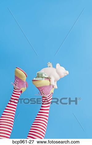 Stock Photo - Legs in striped socks with colorful shoes holding piggy bank. Fotosearch