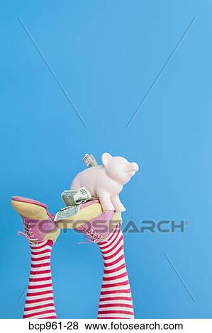 Stock Photo - Legs in striped socks with colorful shoes holding piggy bank. Fotosearch