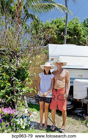 Stock Photo - Man and woman standing in garden with camper. Fotosearch