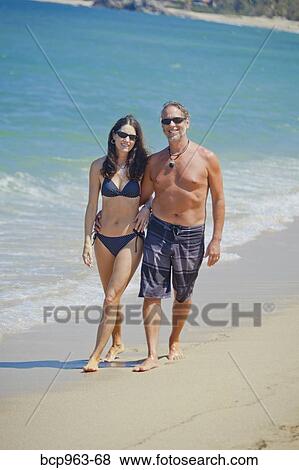 Stock Photo - Man and woman walking on beach in swim suits. Fotosearch