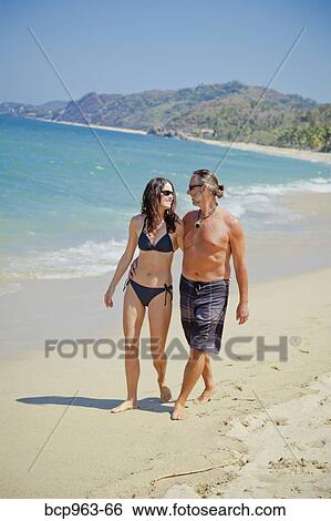 Stock Photograph - Man and woman walking on beach in swim suits. Fotosearch