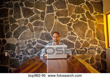 Stock Photography - Man seated at long table with laptop. Fotosearch