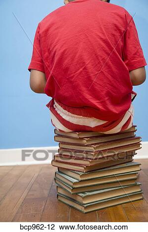 Rear view of boy sitting on stack of books View Large Photo Image Stock Image - Rear view of boy sitting on stack of books. Fotosearch
