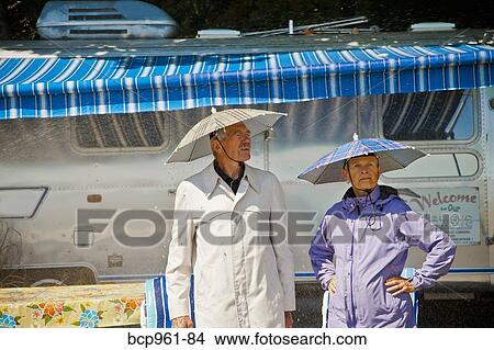 Senior couple in rain hats near airstream camper View Large Photo Image Picture - Senior couple in rain hats near airstream camper. Fotosearch