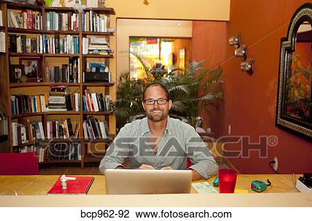 Stock Image - Smiling man seated at desk in home office. Fotosearch