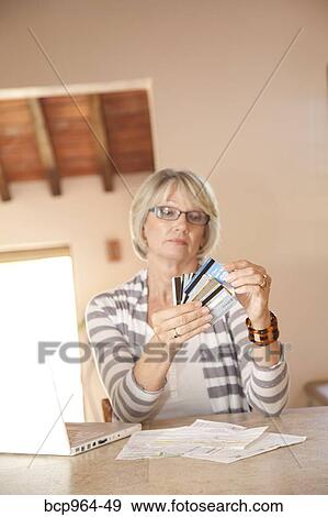 Stock Photo - Woman at home office looking at credit cards. Fotosearch