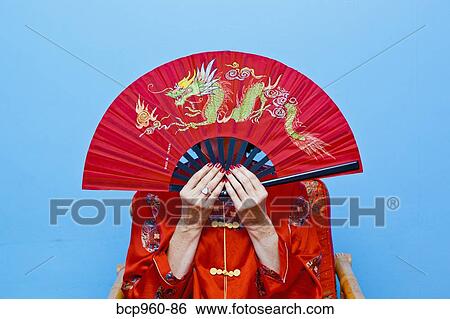 Woman holding red fan in front of her face View Large Photo Image Stock Photograph - Woman holding red fan in front of her face. Fotosearch