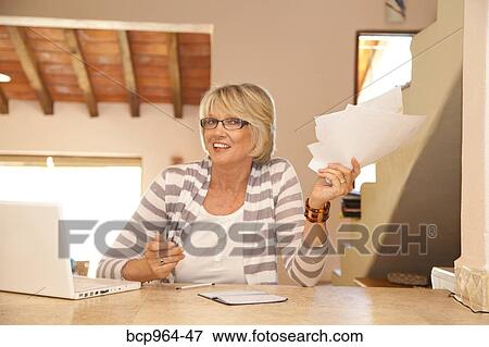 Stock Photo - Woman in home office holding bills. Fotosearch