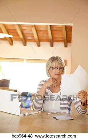 Stock Photo - Woman in home office holding bills. Fotosearch