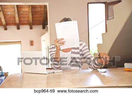 Stock Photo - Woman in home office holding bills. Fotosearch