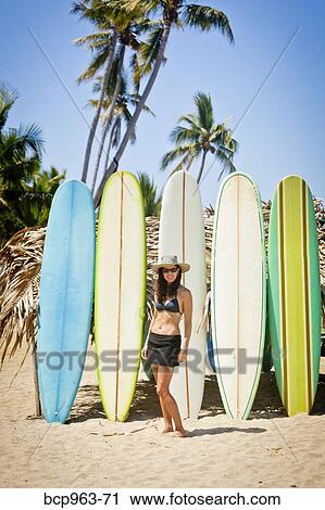 Stock Image - Woman in swimsuit in front of row of surfboards. Fotosearch