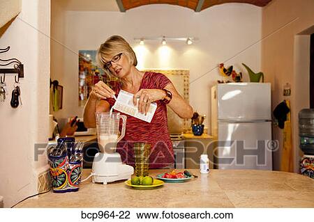 Stock Image - Woman making smoothie in kitchen blender. Fotosearch