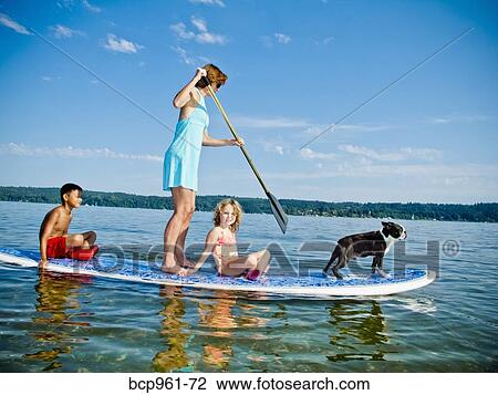 Stock Image - Woman on paddle board with kids and dog. Fotosearch
