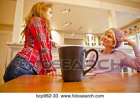 Stock Image - Woman seated at dining table talking with teen girl. Fotosearch