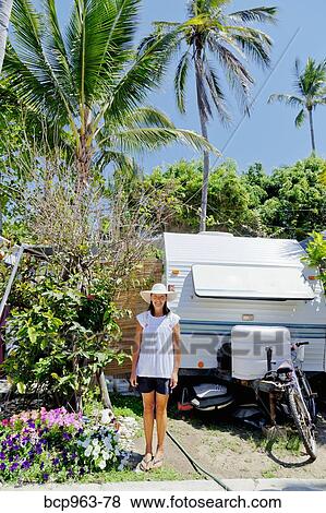 Stock Photo - Woman standing in garden with camper. Fotosearch