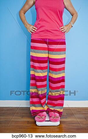 Stock Image - Woman standing on scales. Fotosearch